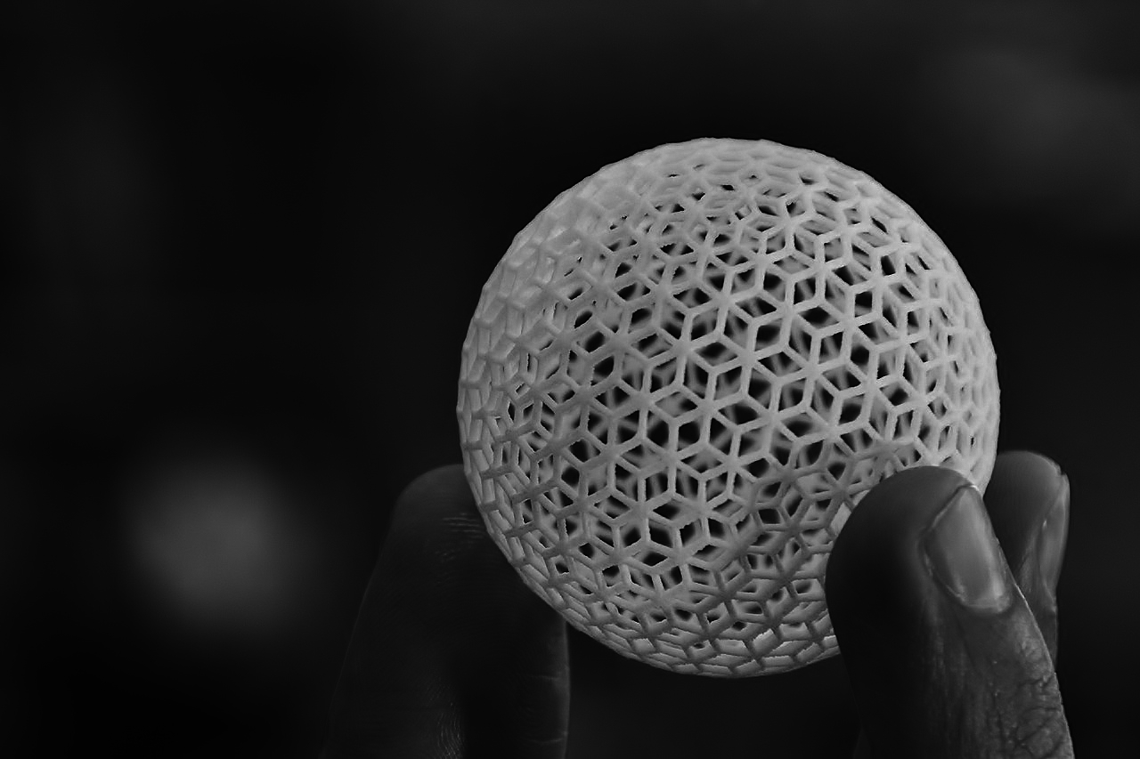 A photograph of a hand holding a hollow 3D printed sphere with a lace like pattern.