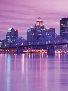 A photograph of a city skyline. There are skyscrapers in the background and a bridge going over water in the forground. The entire photograph is tinted purple. 