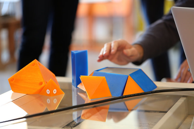 A photograph of a hand reaching for a 3D model.