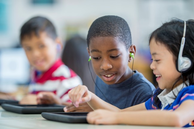 A photograph of Students using a tablet and headphones to read.