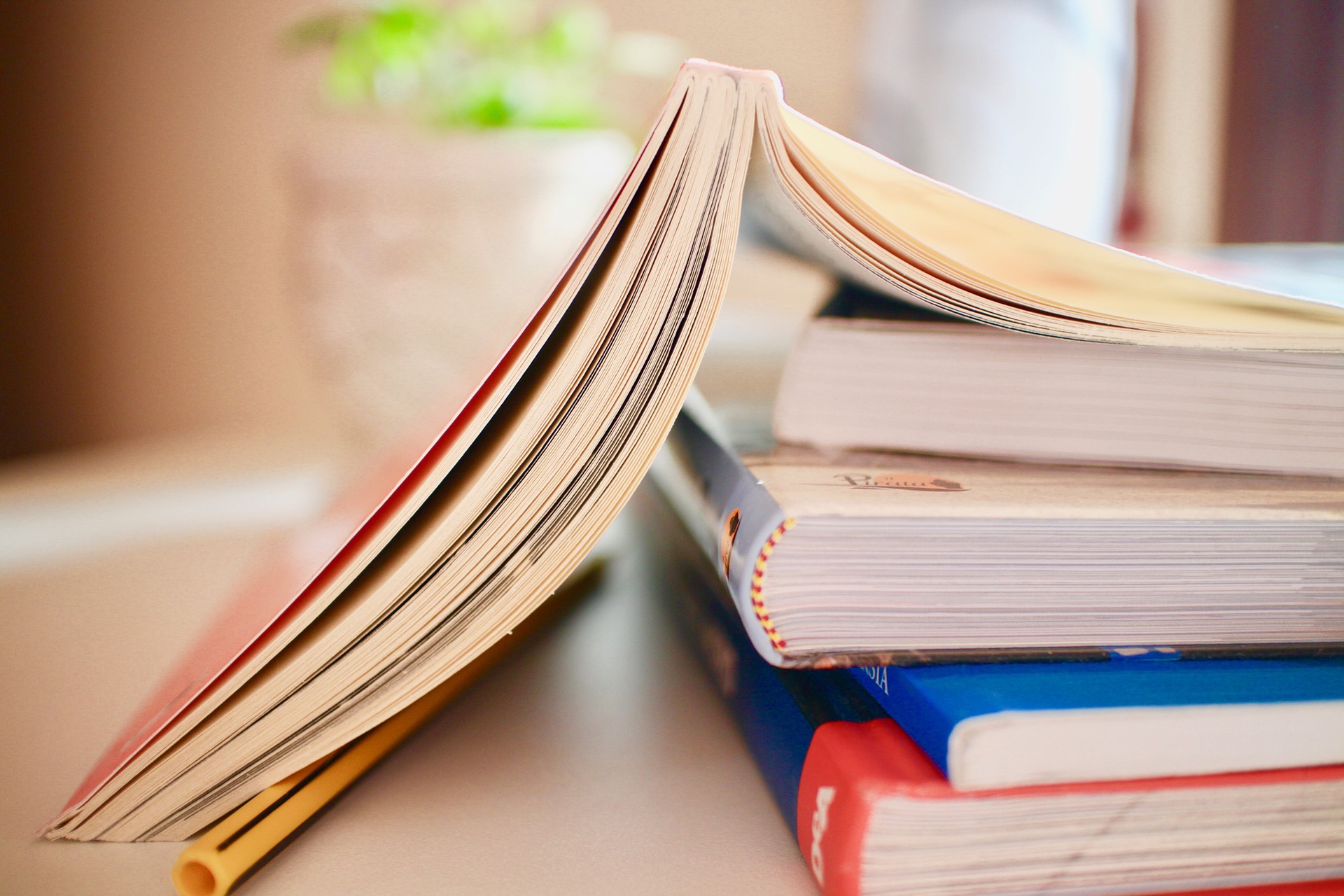 A photograph of a stack of books with the top one open and facing pages down.