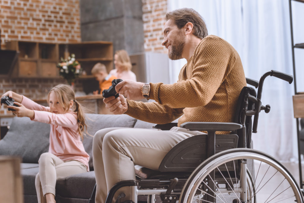 young girl and father in a wheelchair playing video game with wireless controllers.
