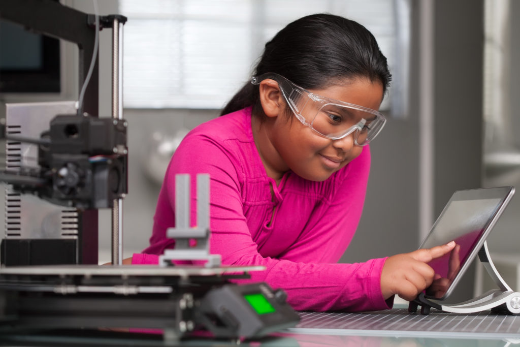 A young student wearing pink is working on a touchscreen making changes to a 3d printed object in a school tech class.